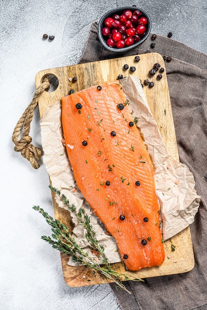 Filete de salmón salado en una tabla de cortar de madera con hierbas y especias. Superficie gris. Vista superior