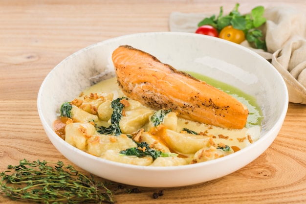 Filete de salmón en salsa de crema con patatas en un plato sobre una superficie de madera clara.