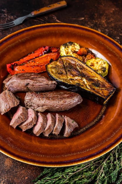 Filete de solomillo de cordero a la plancha Carne, solomillo de cordero en plato rústico con verduras. Fondo oscuro. Vista superior.