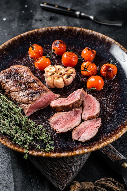 Filete de solomillo de cordero en plato con tomate a la parrilla cordero filete de lomo a la parrilla Fondo negro Vista superior