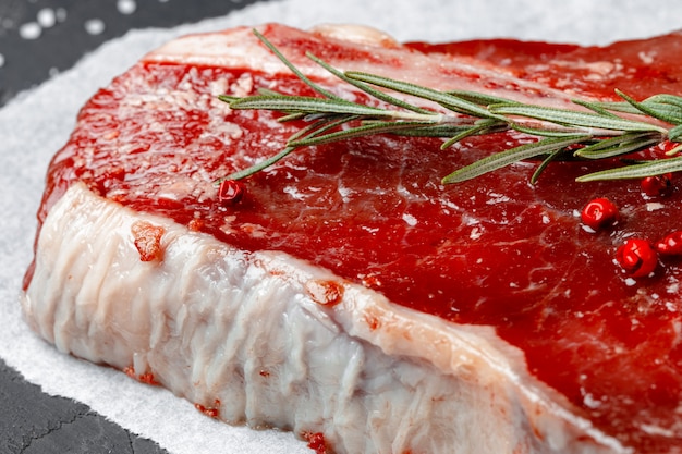 Filete de t-bone de carne fresca cruda con especias sobre un fondo oscuro, de cerca