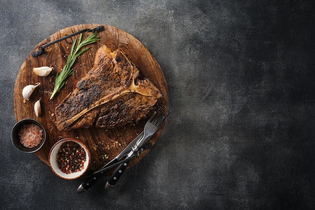 Filete de TBone a la parrilla con sal y pimienta en la tabla de cortar sobre fondo gris oscuro