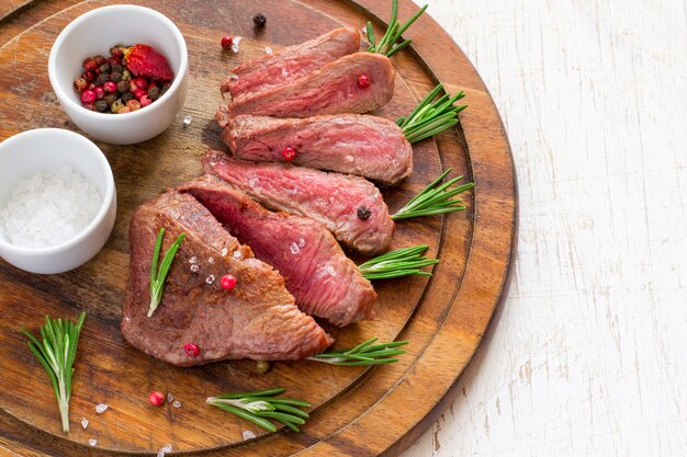 Filete de ternera asado cortado en rodajas con romero sobre tabla de cortar de madera.