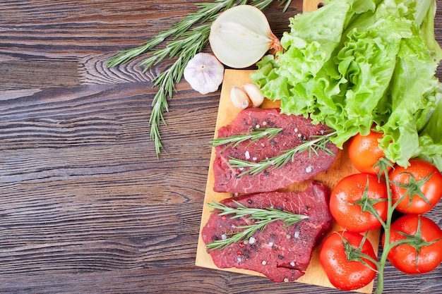 Filete de ternera cruda en tabla de cortar con verduras y especias sobre fondo de madera marrón