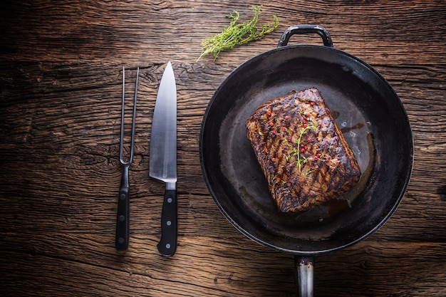 Filete de ternera. Filete de costilla jugoso en sartén sobre tabla de madera con tenedor y cuchillo.