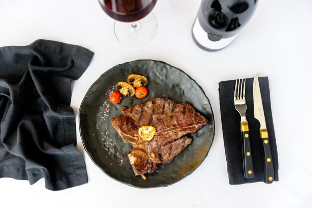 Filete de ternera con hueso en un plato negro con una copa de vino