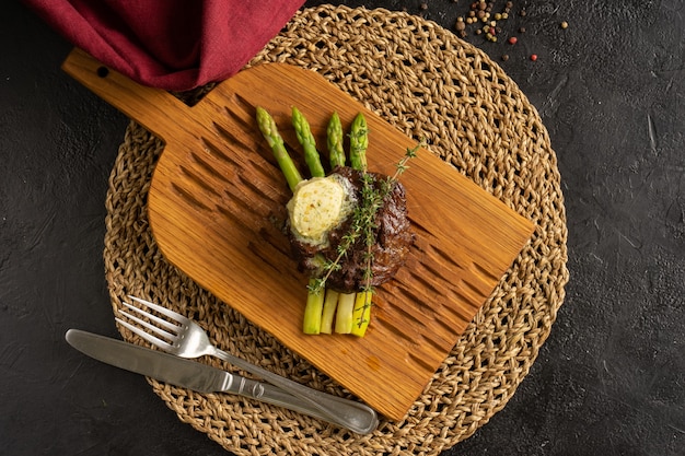 Filete de ternera a la plancha caliente con tomillo, espárragos y mantequilla verde. Un plato caliente de carne y espárragos sobre una tabla de cortar ligera. Vista superior.