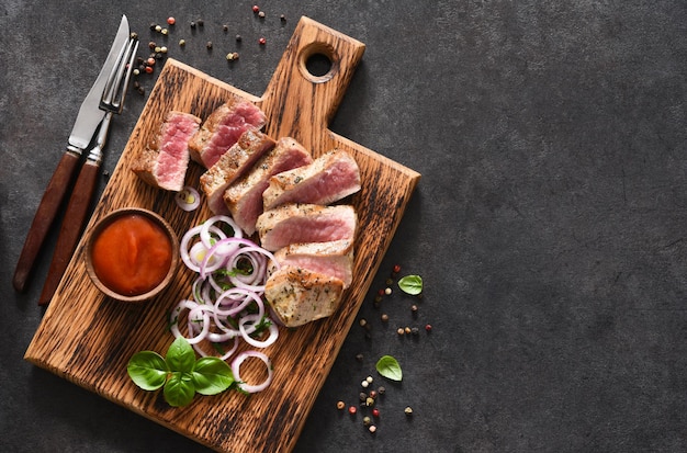 Filete de ternera a la plancha con cebolla y salsa de tomate sobre una tabla de madera. Carne frita.