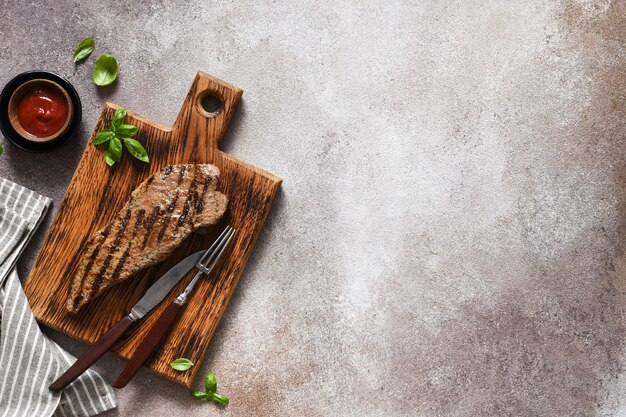 Filete de ternera a la plancha con salsa de tomate sobre una tabla de madera sobre un fondo de hormigón.