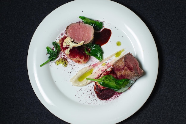 Filete de ternera con puré de patatas decorado con verduras en un plato blanco Sobre un fondo negro Vista superior