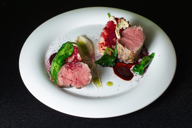 Filete de ternera con puré de patatas decorado con verduras en un plato blanco sobre un fondo negro