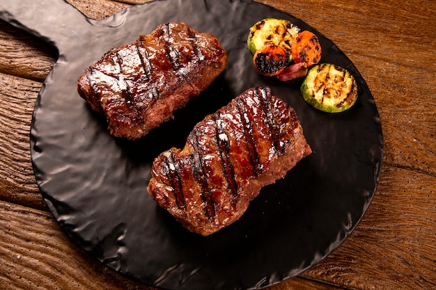 Filete de ternera en rodajas a la parrilla en tabla de cortar en tablero negro sobre la mesa de madera.