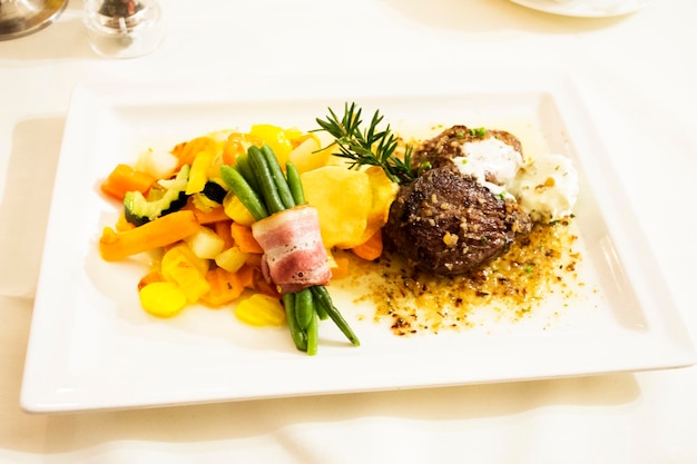 Filete de ternera y salsa de salsa con mezcla de vegetales fritos y jamón enrollado frijol largo en plato de cerámica sirve la cena en el restaurante en el pueblo de Pfunds en Tirol Austria