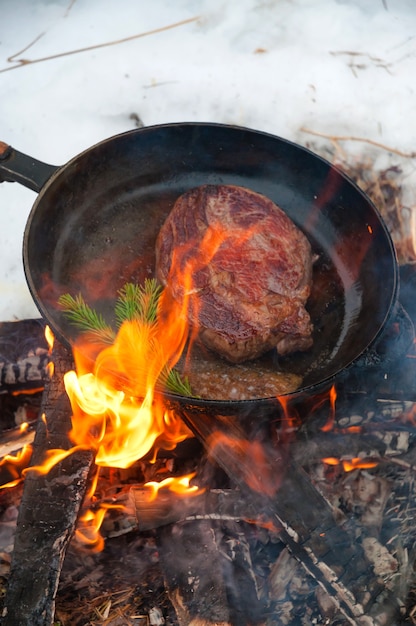 Filete de ternera en una sartén a fuego abierto en un bosque de invierno