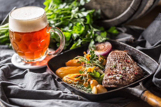 Filete de ternera en sartén a la parrilla con puré de batata, decoración de hierbas de ajo y cerveza de barril.