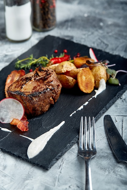 Filete de ternera servido con papas al horno y verduras, superficie negra, primer plano. concepto de comida.