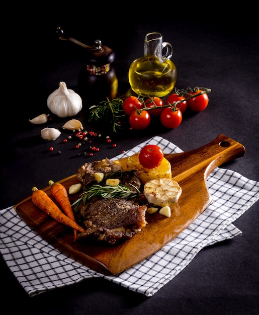 Filete de ternera en una tabla de cortar de madera con verduras y especias sobre fondo negro