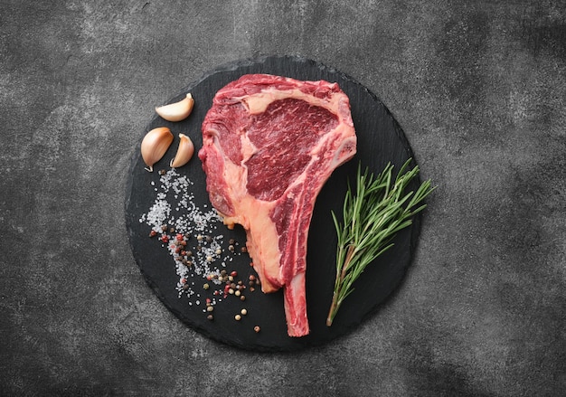 Filete de tomahawk de ternera envejecido seco crudo en tablero de pizarra con especias para parrilla