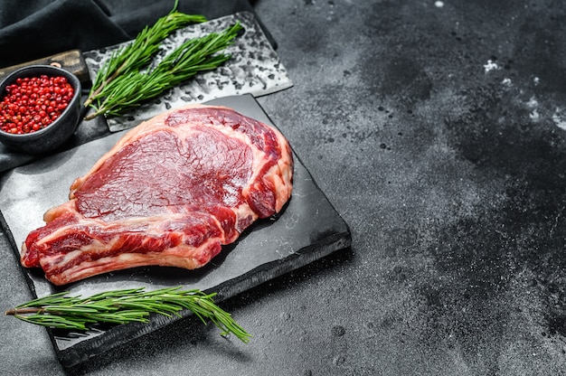 Filete de vaquero crudo. Carne de vacuno de mármol sobre el chuletón de hueso. Fondo negro. Vista superior. Copie el espacio.