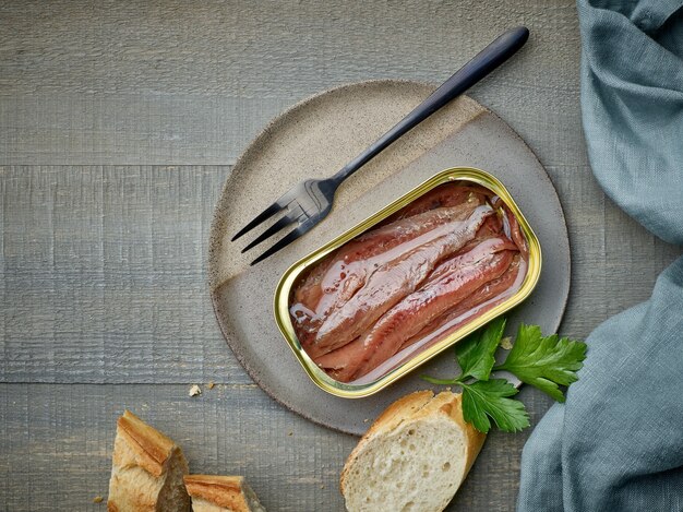 Filetes de anchoa enlatados y rebanadas de baguette en la mesa de la cocina de madera, vista superior