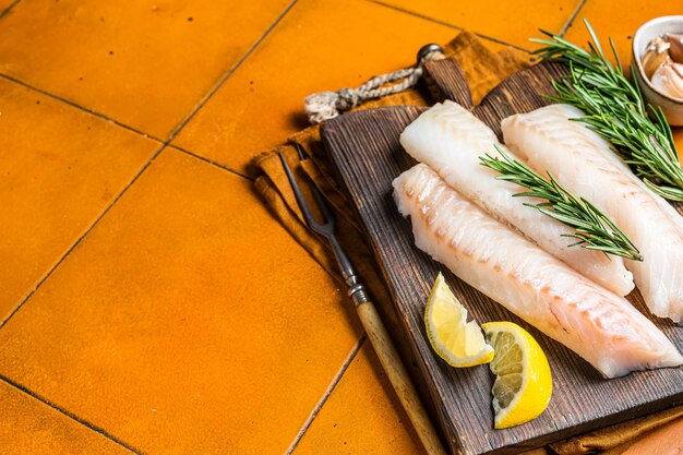 Foto filetes de bacalao crudo bacalao con romero sobre tabla de madera fondo naranja vista superior espacio de copia