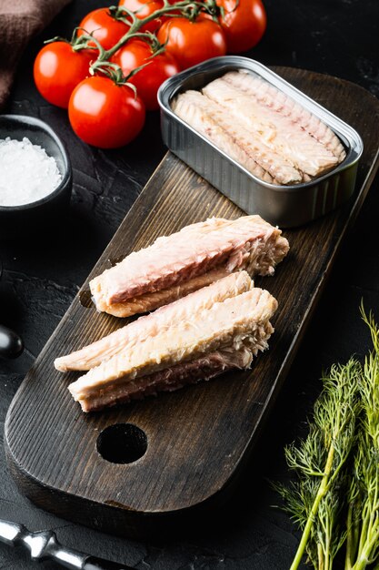 Filetes de caballa en conserva en lata, sobre tabla de cortar de madera, sobre negro