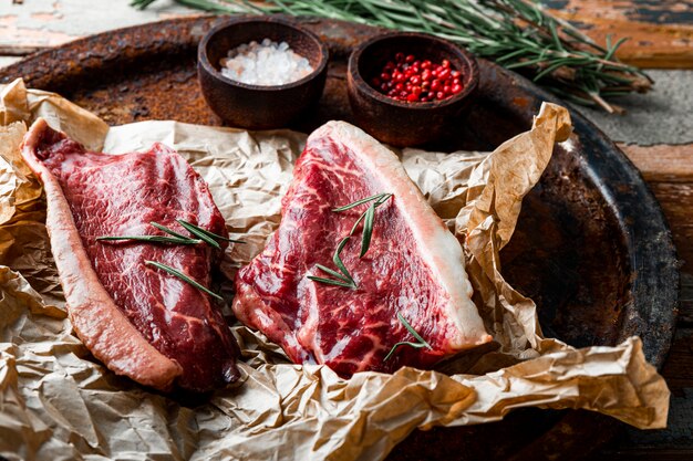 Filetes de carne cruda de mármol y condimentos para su preparación en el fondo de madera vieja. Carne de res cruda en la mesa de la cocina. Foto de alta calidad