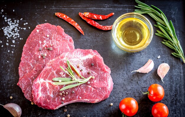 Filetes de carne fresca con ingredientes en el fondo oscuro