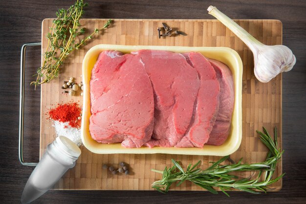 Filetes de carne de ternera cruda y fresca con condimentos en una fila listos para cocinar