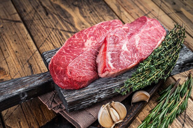 Filetes de carne de vacuno de paletilla cruda en un tablero de carnicero de madera con hierbas. fondo de madera. Vista superior.