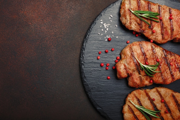 Filetes de cerdo a la parrilla en piedra con romero y pimienta rad sobre fondo oxidado