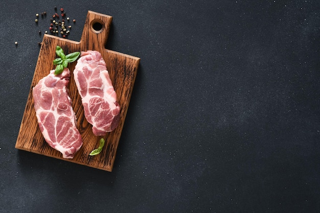 Filetes de cerdo sobre una tabla de madera sobre un fondo negro con especias. Carne cruda fresca.