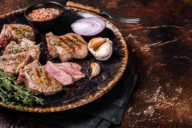 Filetes de chuletas de lomo de cordero a la parrilla, montura en un plato con hierbas. Fondo oscuro. Vista superior. Copie el espacio.