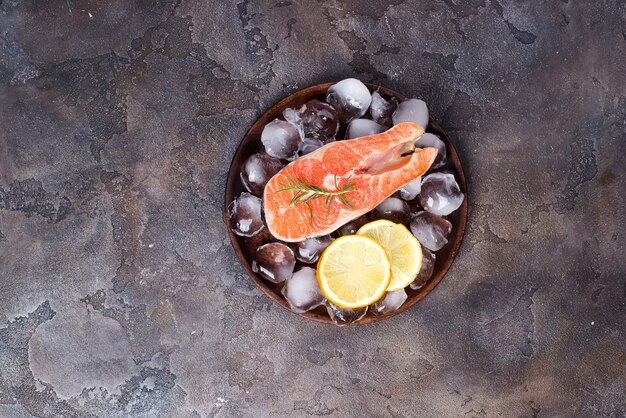 Filetes de color salmón en el hielo con la rebanada del limón en la placa de madera. Proteínas magras.