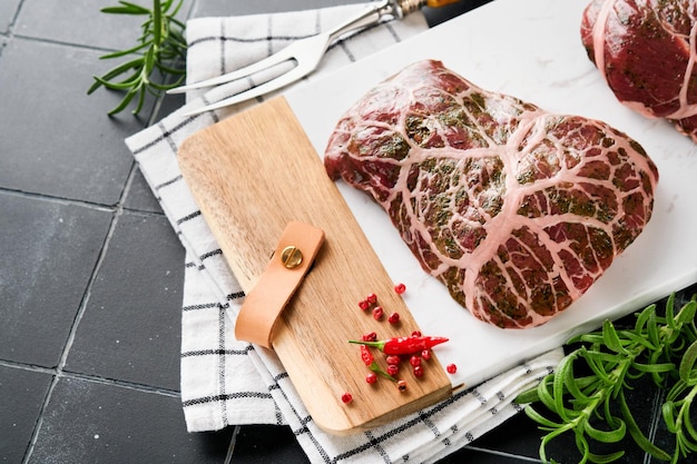 Filetes crudos bistec de vaquero crudo carne de res veteada con especias romero y pimienta sobre pizarra de mármol blanco y fondo de mesa gris Vista superior Maqueta