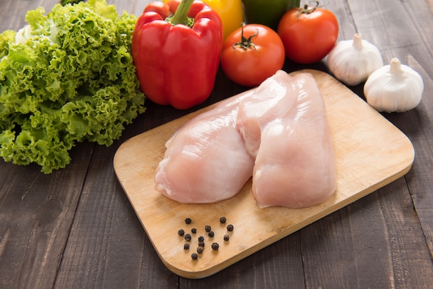 Filetes de peito de frango cru e vegetais na madeira