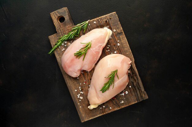 Filetes de peito de frango cru, prontos para cozinhar sobre uma tábua de madeira com especiarias. com espaço de cópia para o seu teste