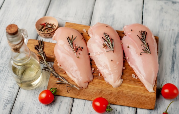 Filetes de peito de frango cru, prontos para cozinhar sobre uma tábua de madeira com especiarias.