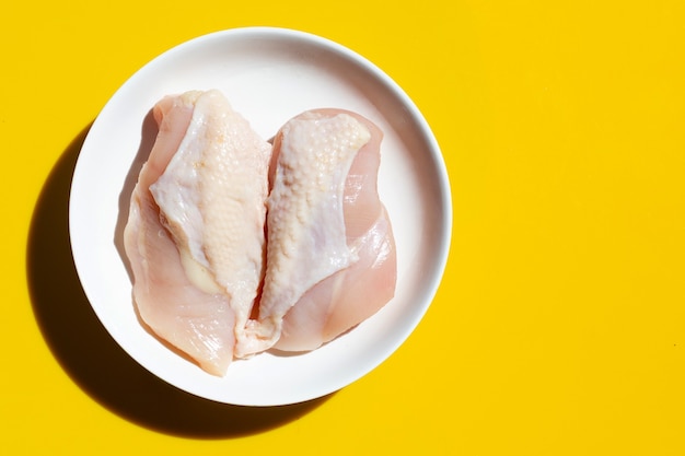 Filetes de peito de frango crus crus sobre fundo amarelo.