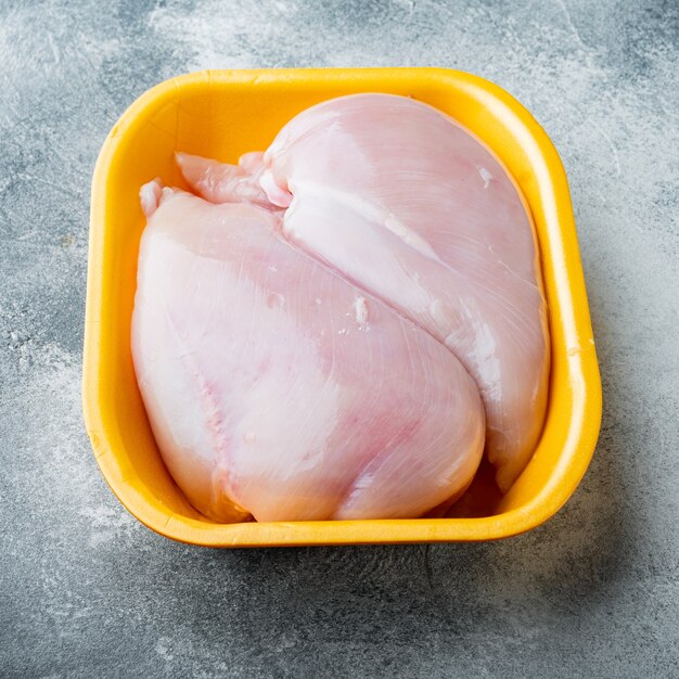 Filetes de peito de frango crus na bandeja, em fundo cinza