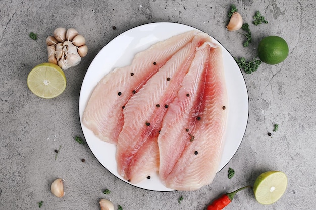 Filetes de peixe branco prontos para cozinhar em prato branco com limão e pimenta sobre um backg cinza