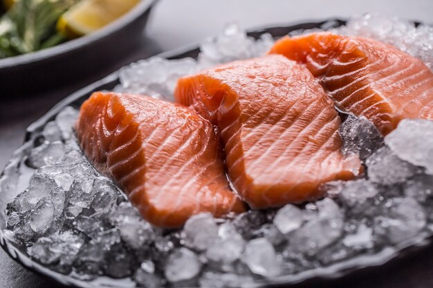 Filetes de salmão crus repartidos no gelo no prato com limão e alecrim.