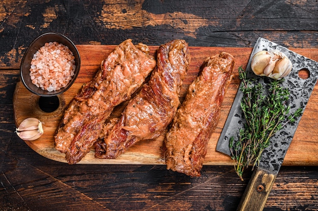 Filetes de falda marinados crudos en salsa barbacoa sobre una tabla de cortar de madera con hierbas. Fondo de madera oscura. Vista superior.