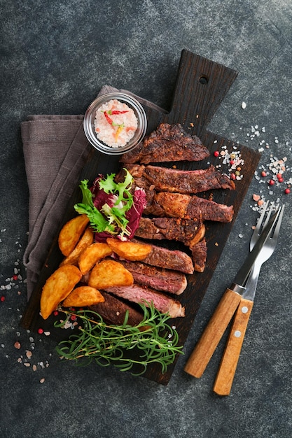 Filetes Filete de carne a la parrilla en rodajas New York Ribeye o Chuck roll con guarnición de ensalada y papas fritas en tablero de mármol negro sobre fondo de madera vieja Vista superior Maqueta