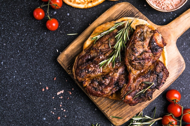 Filetes Filete de carne a la parrilla en rodajas Nueva York o Ribeye con especias, romero y pimienta en tablero negro Vista superior