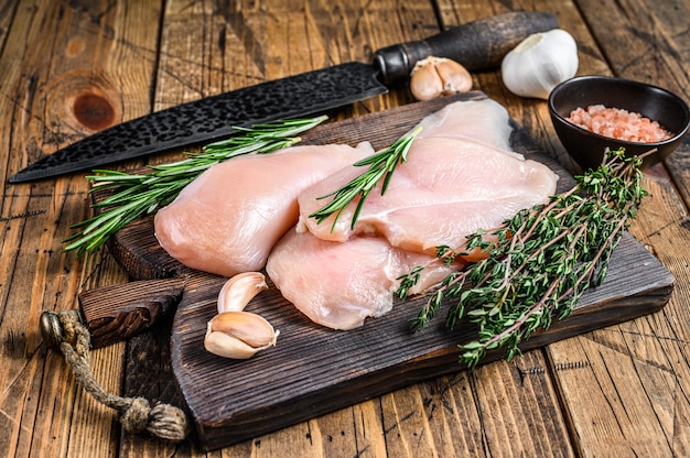 Filetes de filete de pechuga de pollo cortados crudos frescos en una tabla de cortar de madera con un cuchillo de cocina. fondo de madera. Vista superior.