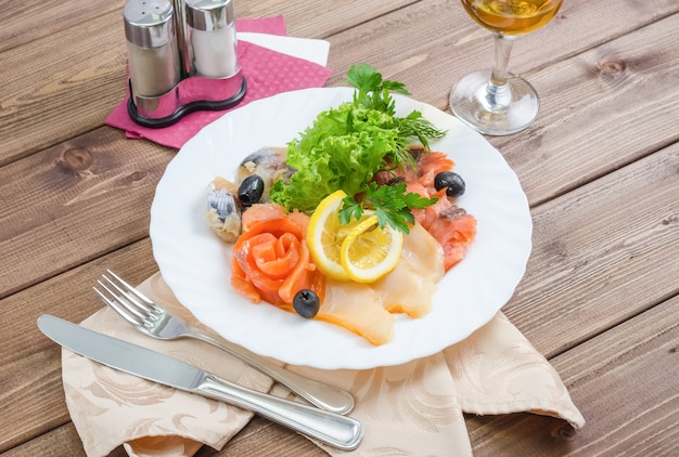 Filetes frescos de diferentes tipos de peixe - vermelho, arenque com limão e alface em um prato branco