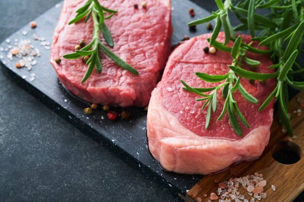 Filetes Fresh Filet mignon Filetes con especias, romero y pimienta sobre tablero de mármol negro sobre fondo gris Vista superior Maqueta