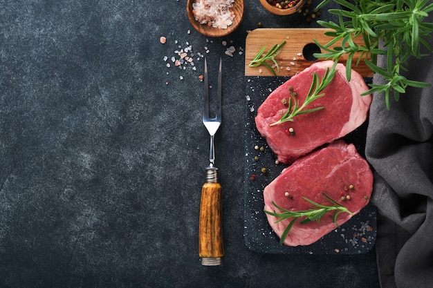 Foto filetes fresh filet mignon filetes con especias, romero y pimienta sobre tablero de mármol negro sobre fondo gris vista superior