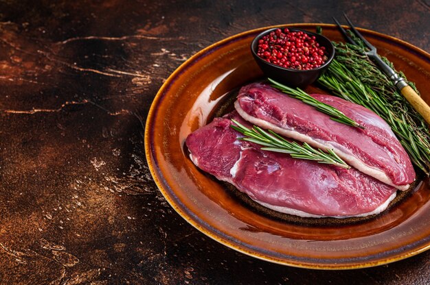 Filetes de pechuga de pato cruda en plato rústico con romero